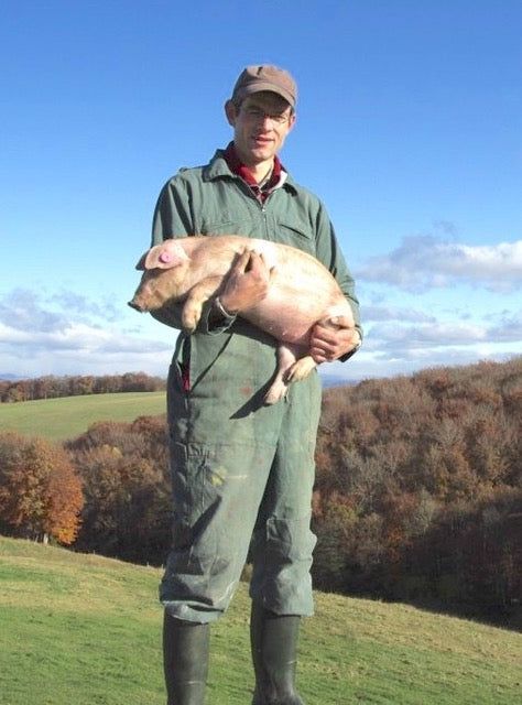 Un éleveur tenant un porcelet dans ses bras, dans un pâturage de montagne en automne.